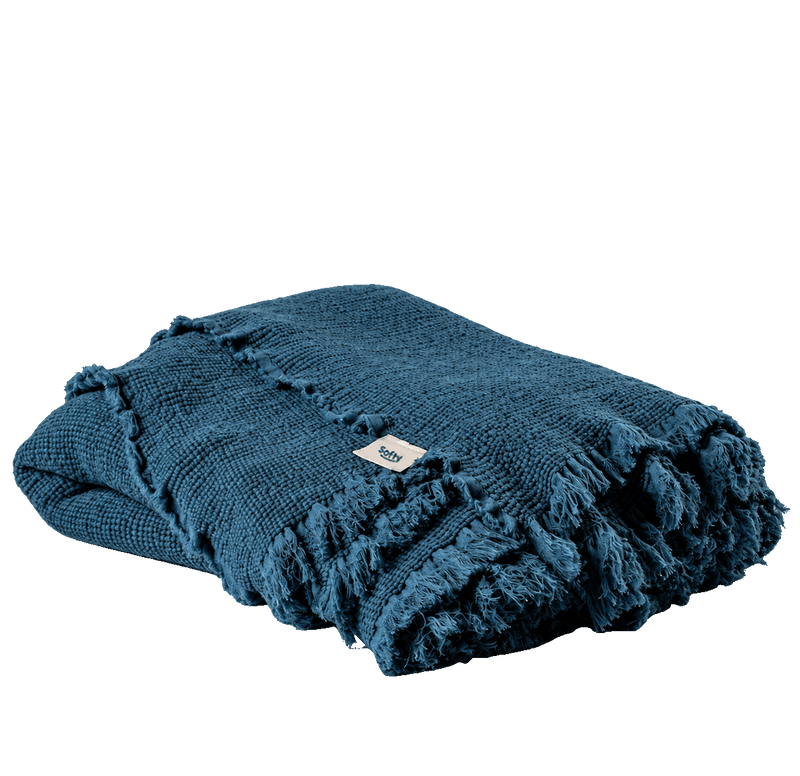 A folded dark teal blue knit throw blanket with fringed edges and a small white brand tag, shown on a plain white background.
